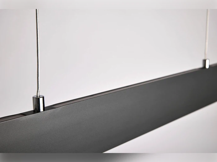 Nærbillede af en moderne, rektangulær sort pendel ophængt i to tynde ledninger mod en almindelig, lys baggrund.