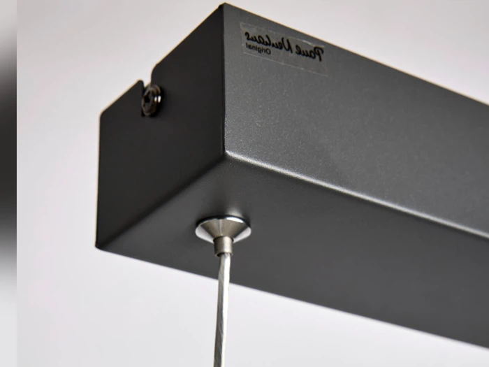 Nærbillede af et sort rektangulært metalarmatur med et hængende kabel på undersiden og en lille etiket på siden, hvor der står True Values original.