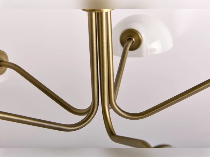 Nærbillede af en moderne lysekrone med guldfarvede metalarme og hvide kuppelformede lysarmaturer på en almindelig lys baggrund.