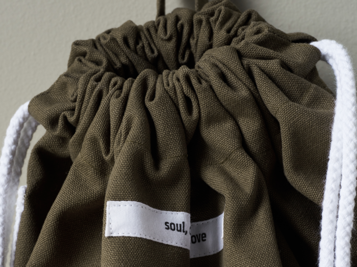 Nærbillede af en olivengrøn taske med snøre og hvide remme og en delvis synlig etiket med teksten soul, ove.