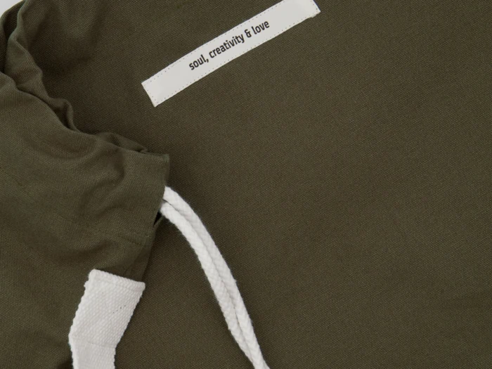Nærbillede af en olivengrøn stofpose med hvide snore og en hvid etiket, hvor der står soul, creativity & love.