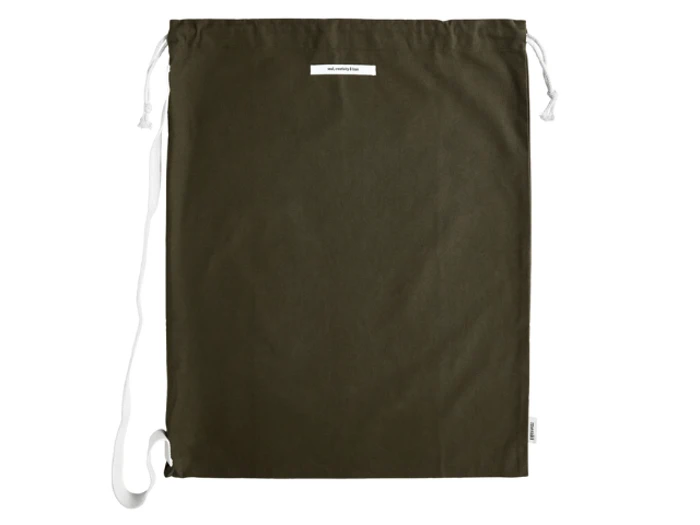 En mørkegrøn pose med snøre, hvid etiket og hvide stropper, lagt fladt på en hvid baggrund.