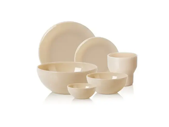 Et sæt med seks cremefarvede keramikfade, herunder tre skåle, to tallerkener og et krus, arrangeret på en hvid baggrund.