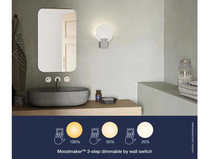 Moderne badeværelse med et rundt spejl, håndvask, håndklæde og Moodmaker-væglampe over vasken; infografikken viser, at lyset kan dæmpes til 100 %, 50 % eller 20 % lysstyrke med en vægkontakt.