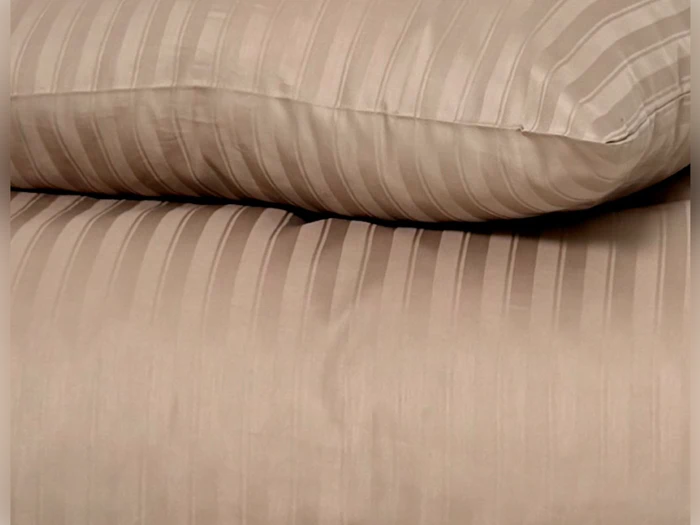 Et nærbillede af en beige pude, der hviler på en matchende beige dyne, begge med diskrete lodrette striber.