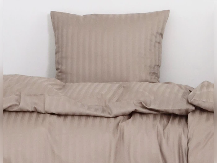 En pænt redt seng med en beige, stribet pude og matchende dyne mod en almindelig hvid væg.