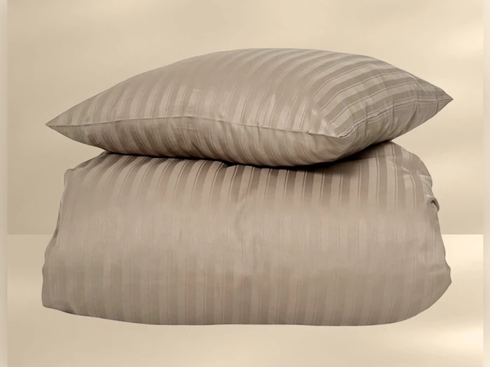 En beige, stribet pude hviler oven på en matchende stribet dyne på en neutral baggrund.