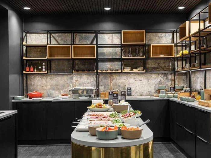 En moderne buffetopstilling i et slankt køkken med sorte skabe, åbne hylder og en række friske madretter arrangeret på en central ø.