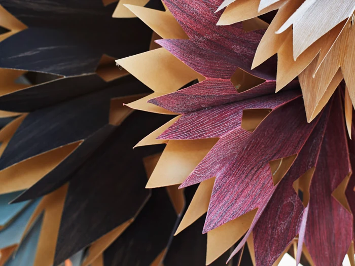Nærbillede af lagdelte, spidse papirformer i brune, sorte og rødlilla nuancer, der ligner abstrakte blade eller kronblade, som overlapper hinanden.