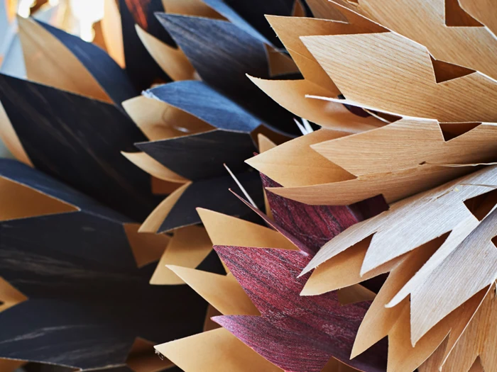 Nærbillede af overlappende, takkede papir- eller papfigurer i brune, sorte og rødbrune nuancer, der ligner abstrakte blomsterblade eller blade.