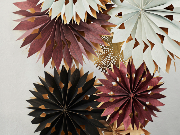 Stjernedekorationer af papir i hvide, bordeaux og sorte farver er arrangeret sammen mod en almindelig lys vægbaggrund.