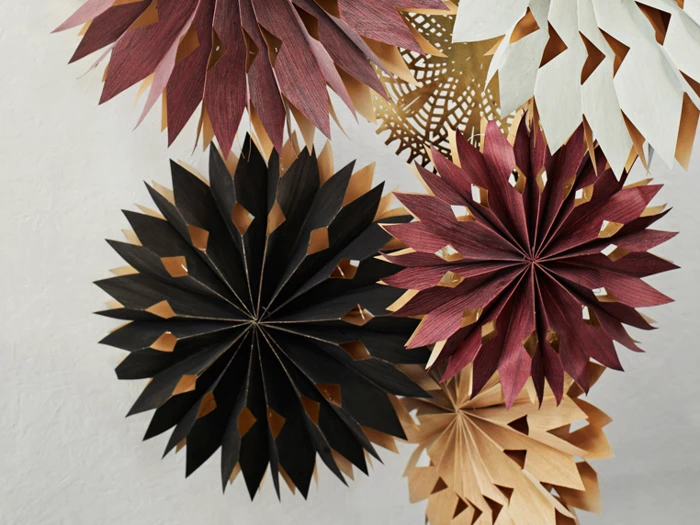 Papirdekorationer i sort, rødbrun, creme og beige, arrangeret i lagdelte, stjerneformede blomster på en almindelig hvid baggrund.