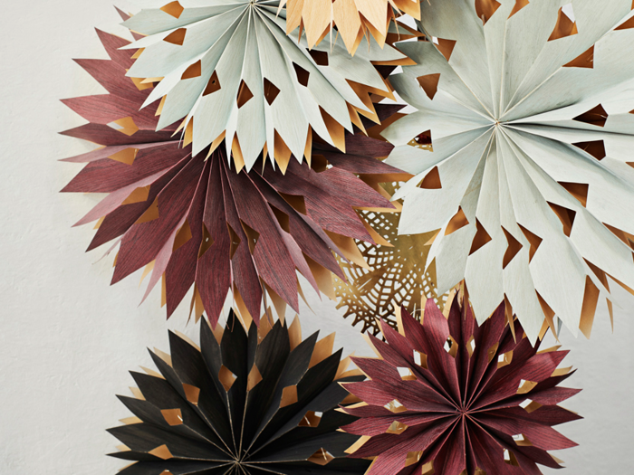 Papirdekorationer med lagdelte, spidse og geometriske mønstre i nuancer af creme, bordeaux, guld og sort er samlet i klynger mod en lys baggrund.