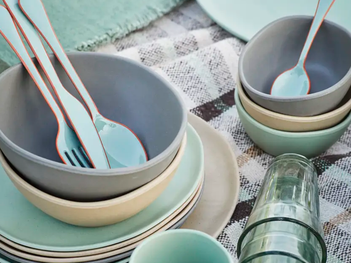 Stablede pastelfarvede skåle, tallerkener og kopper med redskaber indeni, arrangeret på en ternet dug sammen med klare glas.
