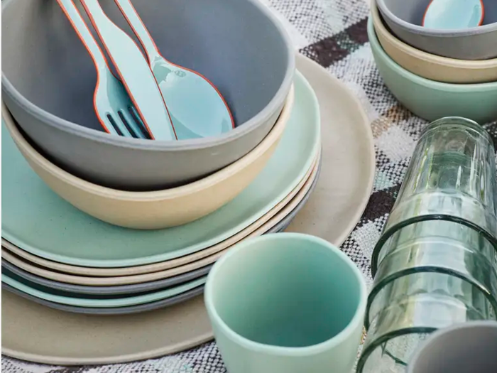 En stak pastelfarvede tallerkener og skåle, matchende kopper, turkis bestik og klare glas arrangeret på en ternet dug.