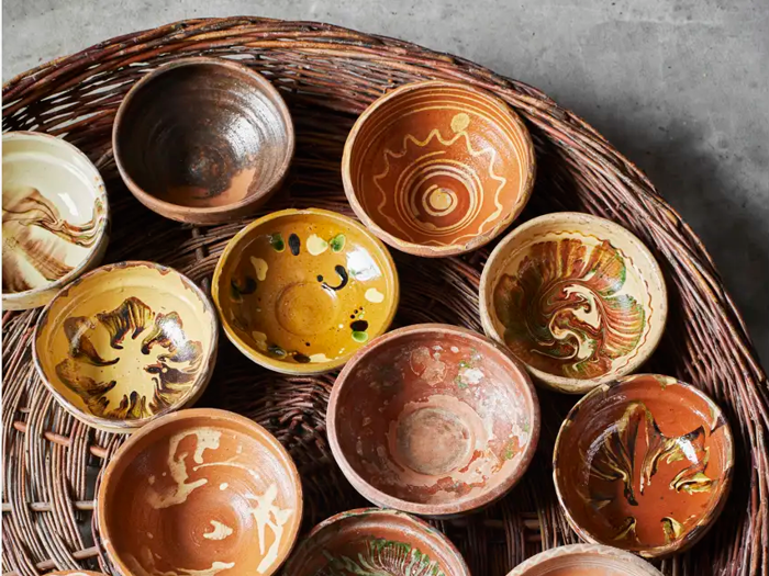 En gruppe håndlavede keramikskåle med forskellige farverige, hvirvlende mønstre arrangeret på en flettet kurveoverflade.