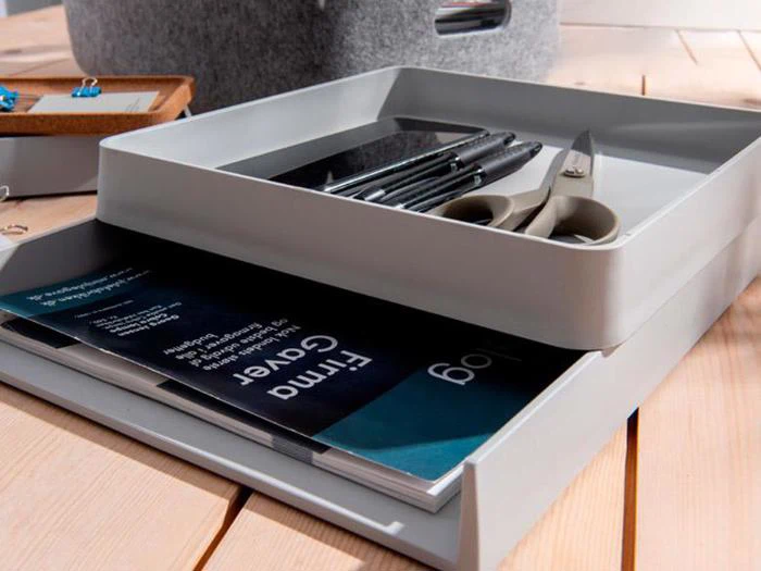 En hvid skrivebordsorganizer har plads til kuglepenne, telefon og saks i den øverste bakke, mens mapper og papirer opbevares i den nederste bakke på et træskrivebord.