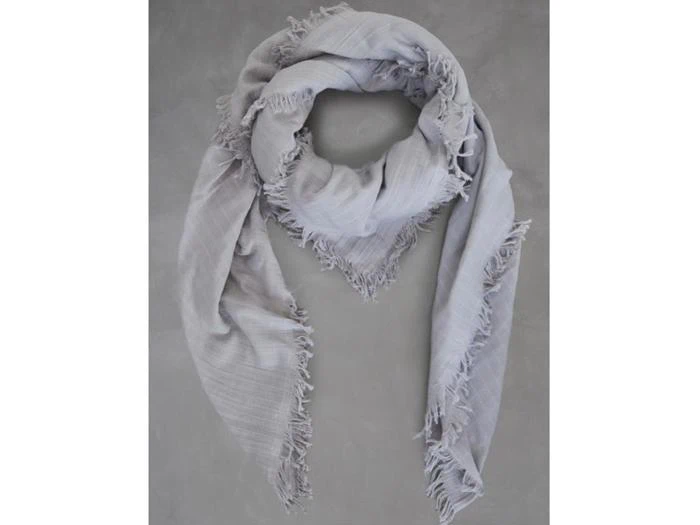 Et lysegråt, trekantet tørklæde med flossede kanter er lagt fladt på en neutral grå baggrund.
