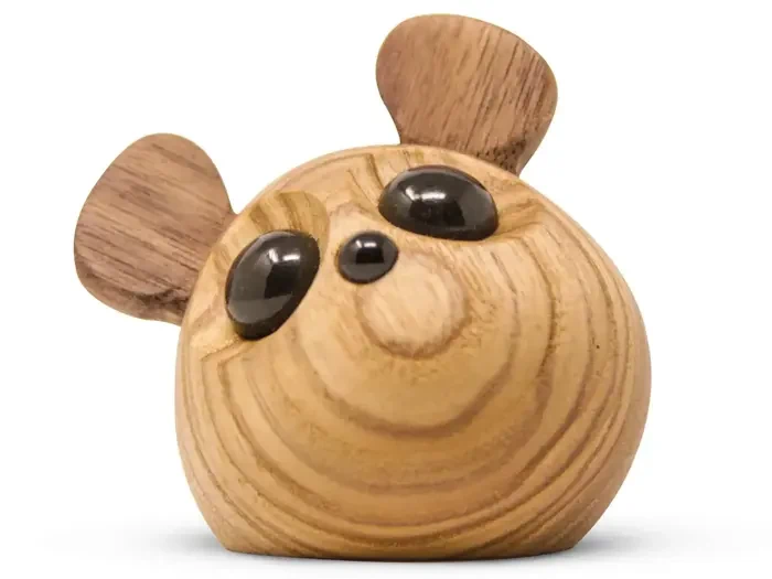 En lille, rund træfigur med store sorte øjne og to udstående træører, der ligner et bjørnehoved, på en hvid baggrund.