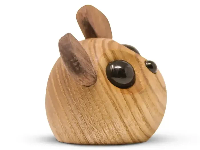 En rund træfigur med to mørke træører og store sorte øjne, der ligner et dyr, muligvis en mus eller en kat, på en hvid baggrund.