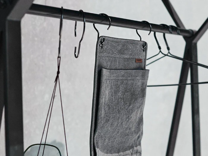 Nærbillede af metalkroge og bøjler, der holder en grå stoforganisator på et sort tøjstativ af metal.