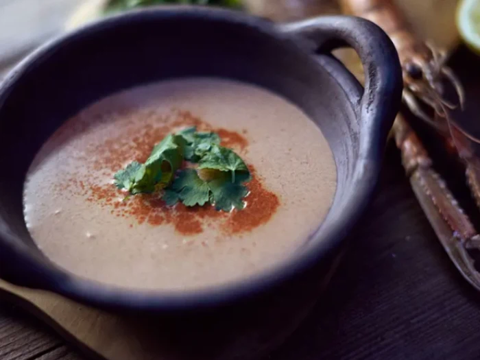 En skål cremet suppe garneret med koriander og et drys rødt krydderi, serveret i en rustik sort skål.