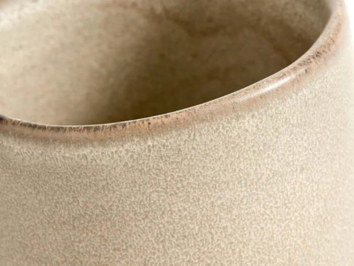 Nærbillede af kanten på en beige, struktureret keramisk kop eller gryde med en glat, let buet kant.