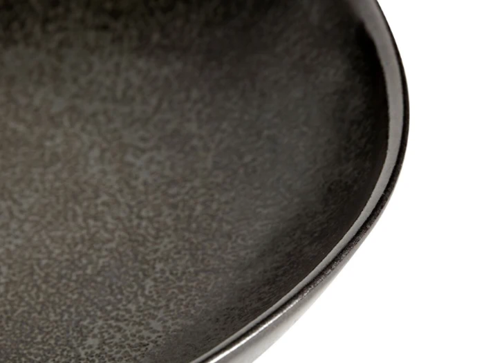 Nærbillede af kanten og den strukturerede indre overflade af en mørk keramikskål, der viser den glatte, buede kant og den spættede finish.