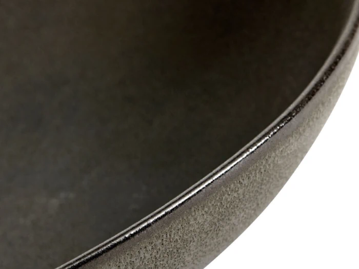 Nærbillede af kanten og overfladen på en mørk, rund keramikskål, der viser dens strukturerede finish og bløde kurve.