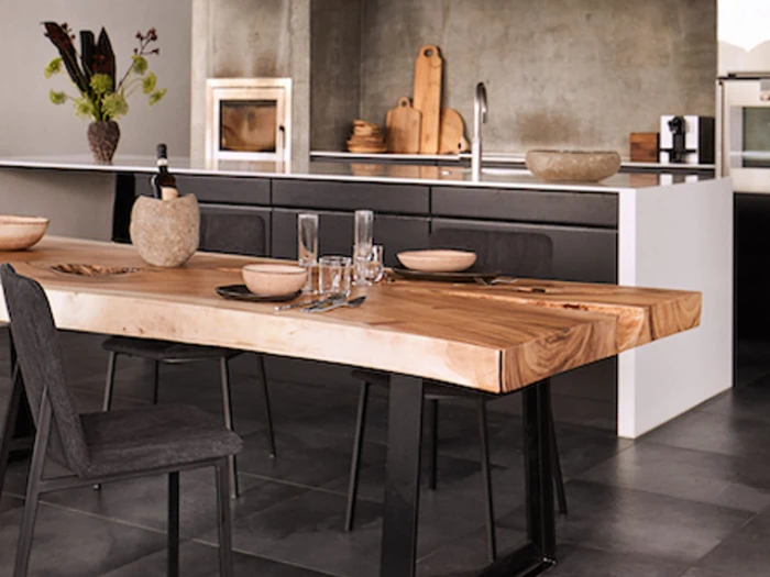 Et moderne køkken med et spisebord i naturtræ, sorte stole, stentøjsfade og et minimalistisk design i grå og hvid.