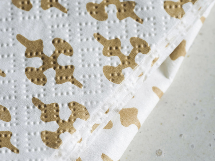 Nærbillede af foldede hvide papirservietter med et brunt abstrakt mønster og struktureret, prikket prægning på en lys overflade.