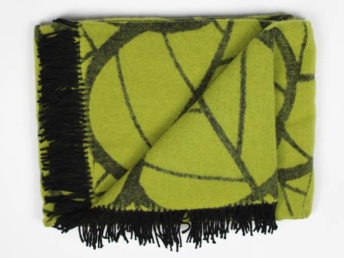 Et foldet grønt tæppe med sorte frynser og et geometrisk sort mønster på en hvid baggrund.