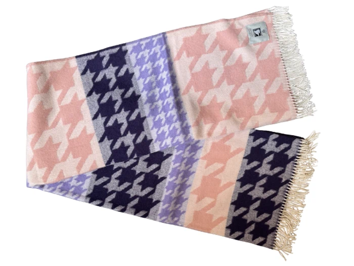 Et blødt tørklæde med pink, lilla og navy houndstooth-mønster og frynser i de hvide ender, lagt fladt med et lille mærke i det ene hjørne.