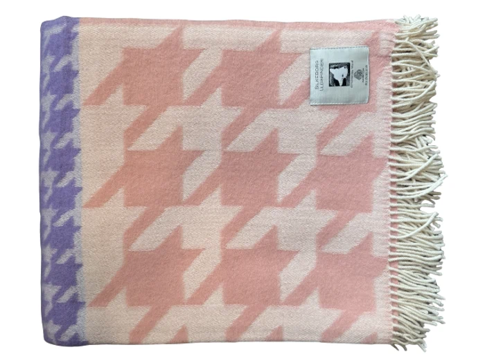 Et lyserødt og lilla houndstooth-mønstret uldtæppe med cremefarvede frynser og et rektangulært mærke syet på det ene hjørne.