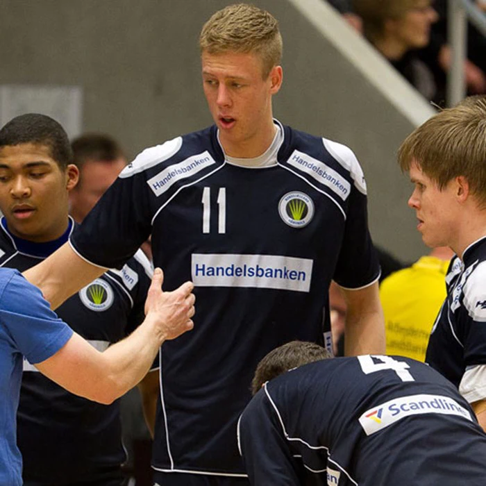 Et volleyballhold i mørke trøjer lytter til en træner under en timeout; spiller nummer 11 skiller sig ud i midten.