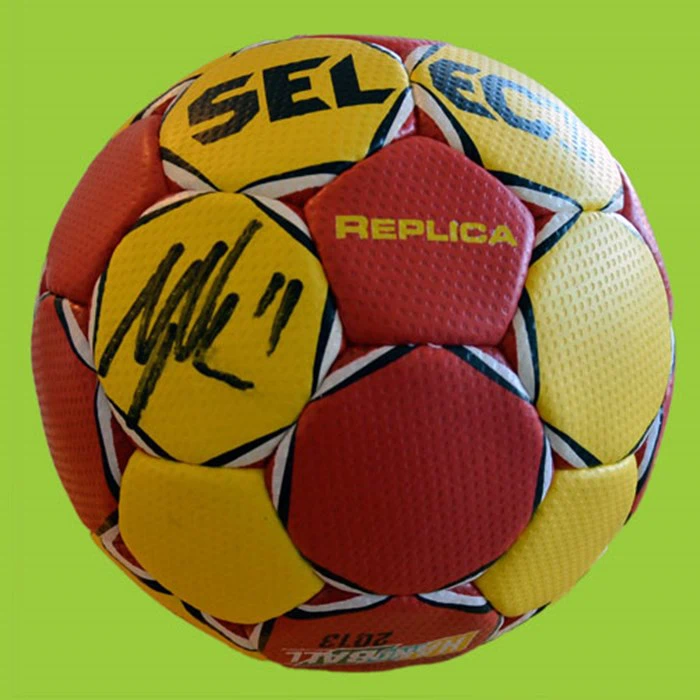 En rød og gul håndbold af mærket SELECT med en sort autograf, ordet REPLICA og en grøn baggrund.