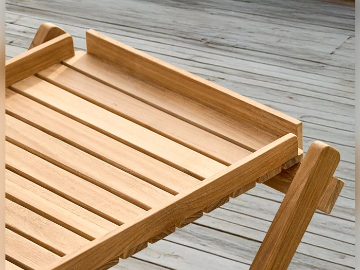 Et nærbillede af et bord med trælameller og hævede kanter, som står på en forvitret træterrasse.