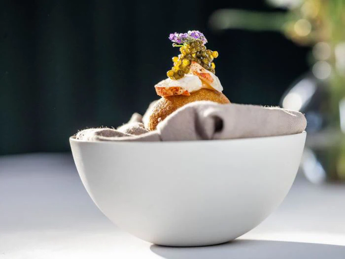 En gourmetforret med kaviar, fløde og krydderurter ligger på en serviet i en hvid skål på en sløret baggrund.