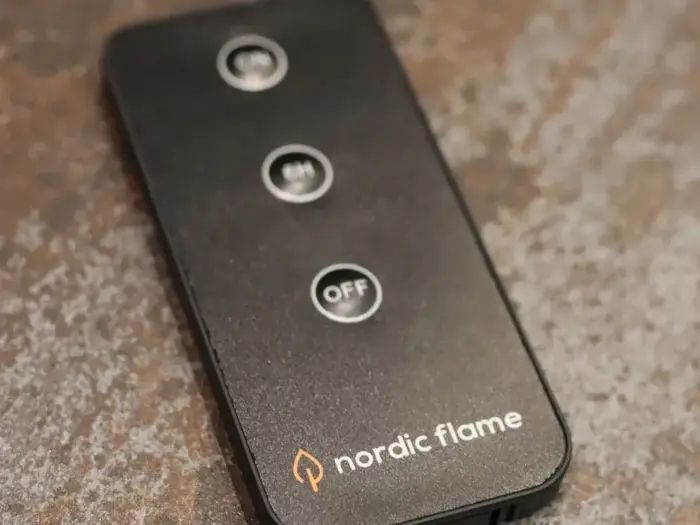 En sort fjernbetjening mærket nordic flame med tre knapper mærket med ikoner, inklusive en fremtrædende OFF-knap i midten.