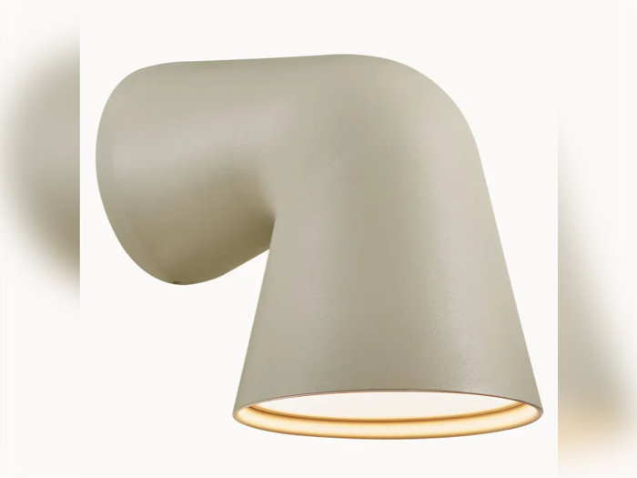 Et moderne vægmonteret lysarmatur med en glat, mat beige finish og et vinklet, cylindrisk design, der udsender lys fra bunden.