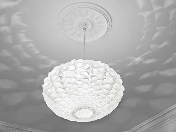 En hvid, struktureret pendel hænger fra et loft og kaster et indviklet mønster af skygger hen over loftets overflade.