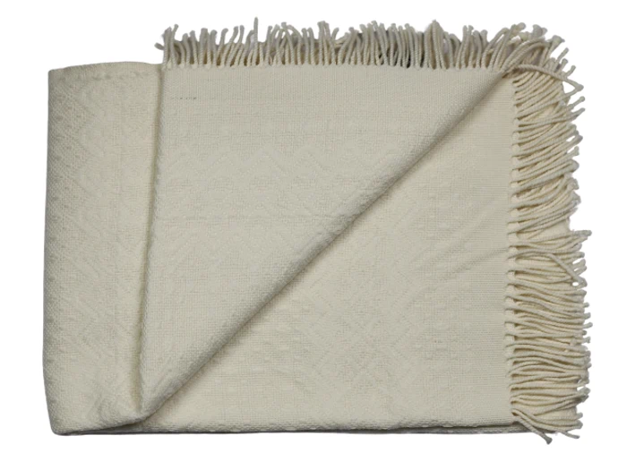 Et cremefarvet vævet tæppe med frynsede kanter, pænt foldet med det ene hjørne vendt om for at vise strukturen.