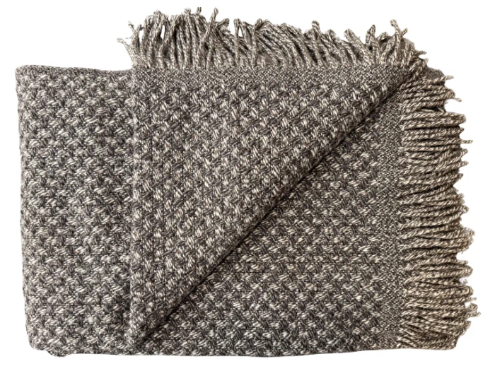 Et foldet vævet gråt og hvidt tæppe med et struktureret mønster og frynsede kanter, vist på en hvid baggrund.
