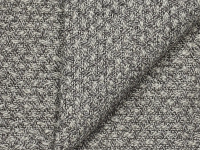 Nærbillede af et foldet stof med et struktureret, vævet mønster i grå og hvide nuancer, der viser detaljerede tråde og syninger.