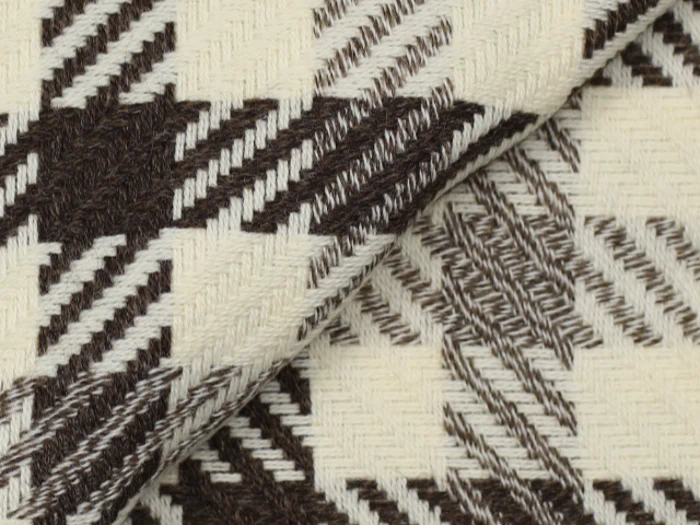 Nærbillede af et vævet stof med et geometrisk zigzagmønster i mørkebrune og cremefarvede nuancer, der viser tekstur og overlappende lag.