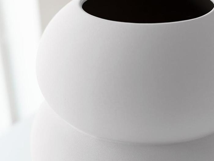 Nærbillede af en glat, hvid, afrundet vase med en bred åbning i toppen, vist i blødt, naturligt lys.