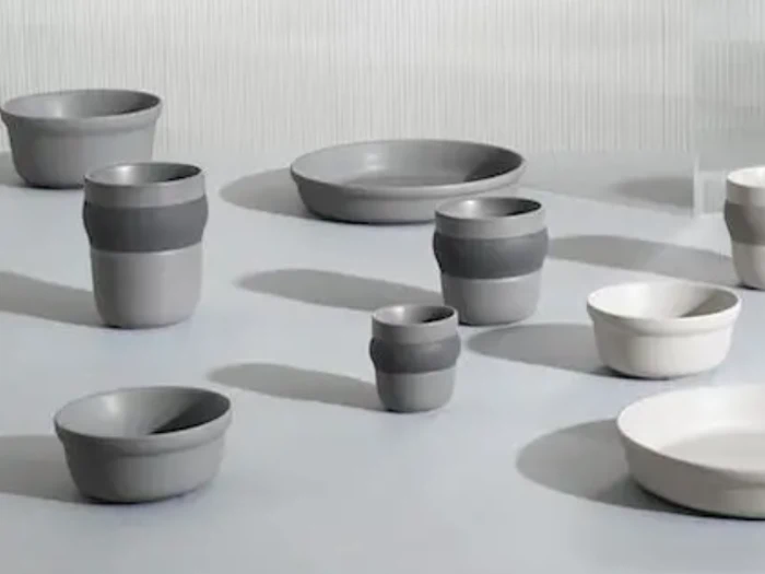 En samling af moderne, minimalistiske keramikskåle og kopper i grå og hvide nuancer arrangeret på en lys overflade.