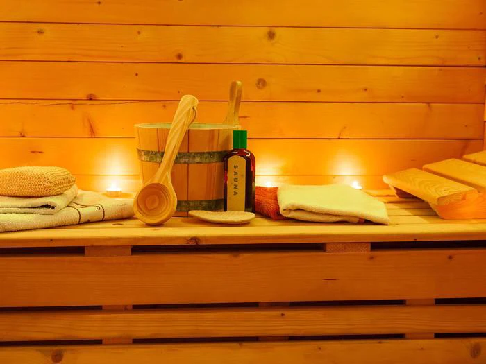 Et sauna-interiør i træ med spand, øse, håndklæder, olieflaske og stearinlys skaber en varm og afslappende atmosfære.