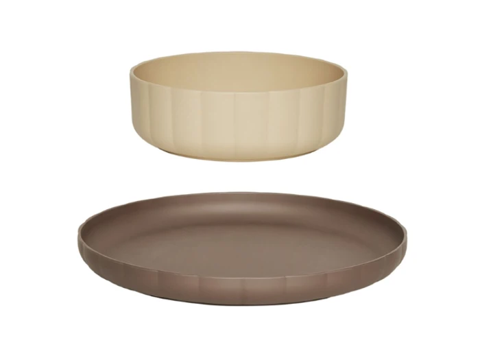 En beige, rund skål sidder over en flad, brun tallerken, begge med diskrete lodrette riller, mod en hvid baggrund.