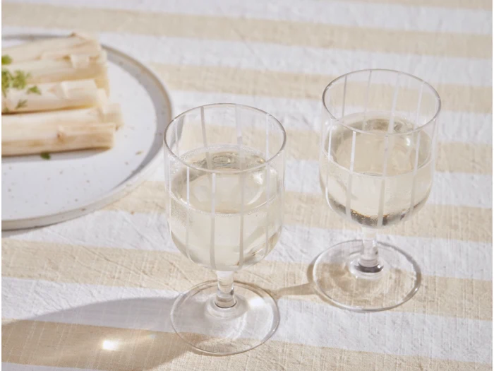 To glas hvidvin står på en stribet dug ved siden af en tallerken med hvide asparges.
